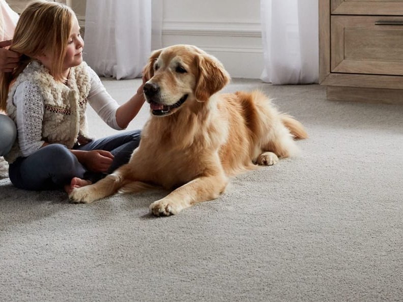 Mother and daughter sitting on carpeted floor with dog